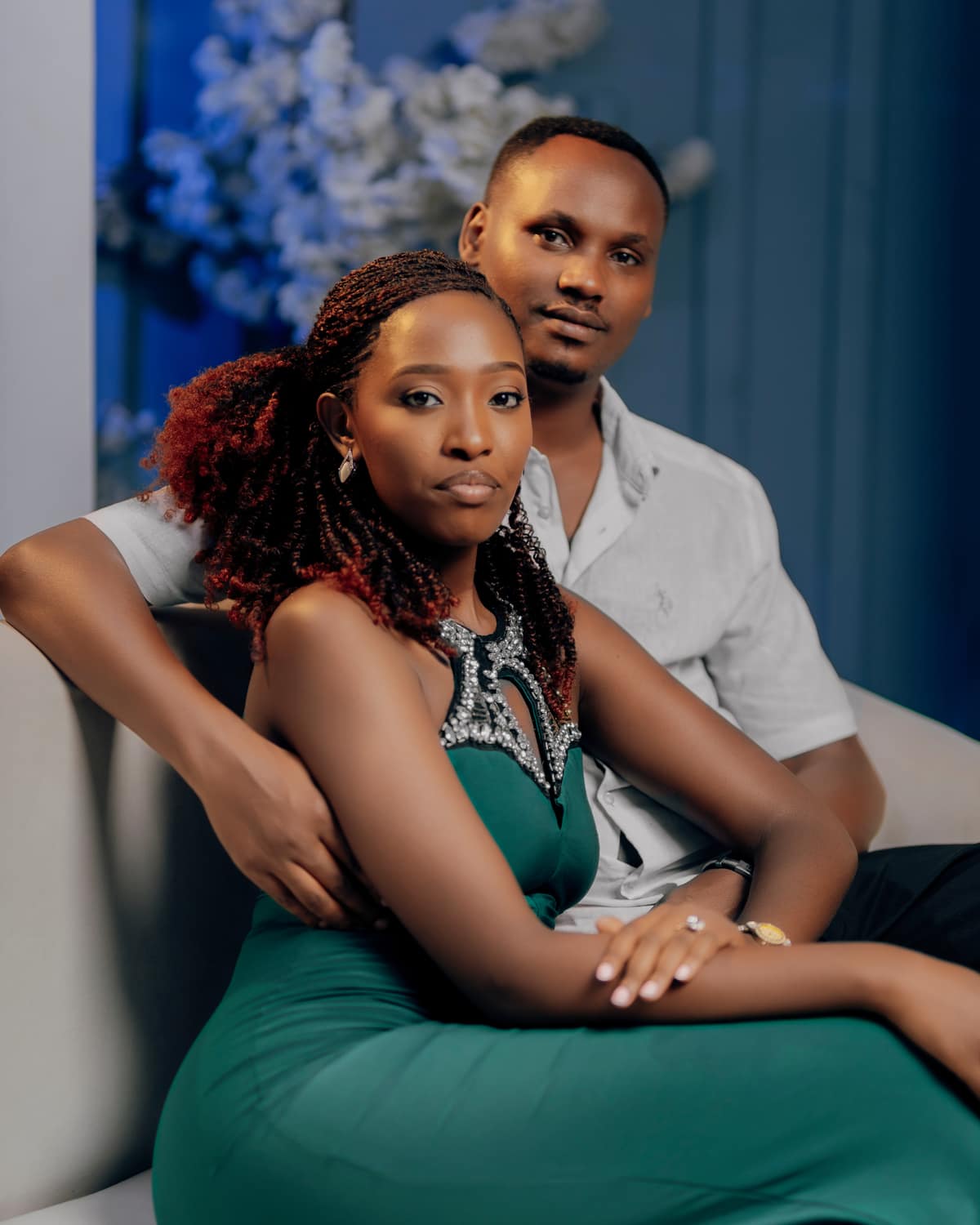 Celine in an emerald gown seated in front of Khalim, his arms around her